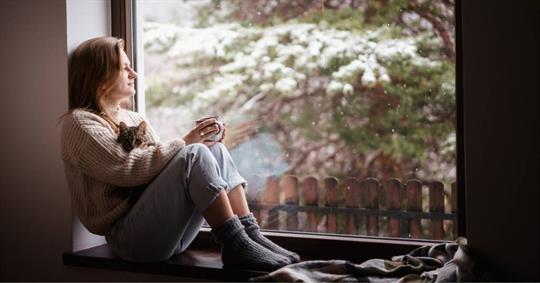 Woman  sitting at home on the windowsill in a warm sweater drinking coffee