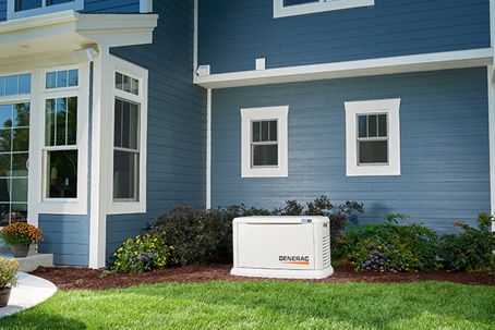 A light-colored generator sits on the lawn next to a blue house.