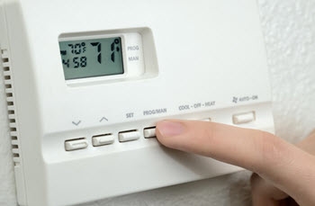 A finger presses the "PROGRAM" button on a thermostat.