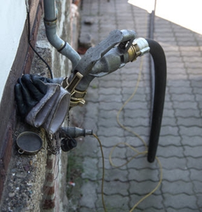 A picture depicts a black hose and metallic pipe connected outside with a hand-held nozzle attached.